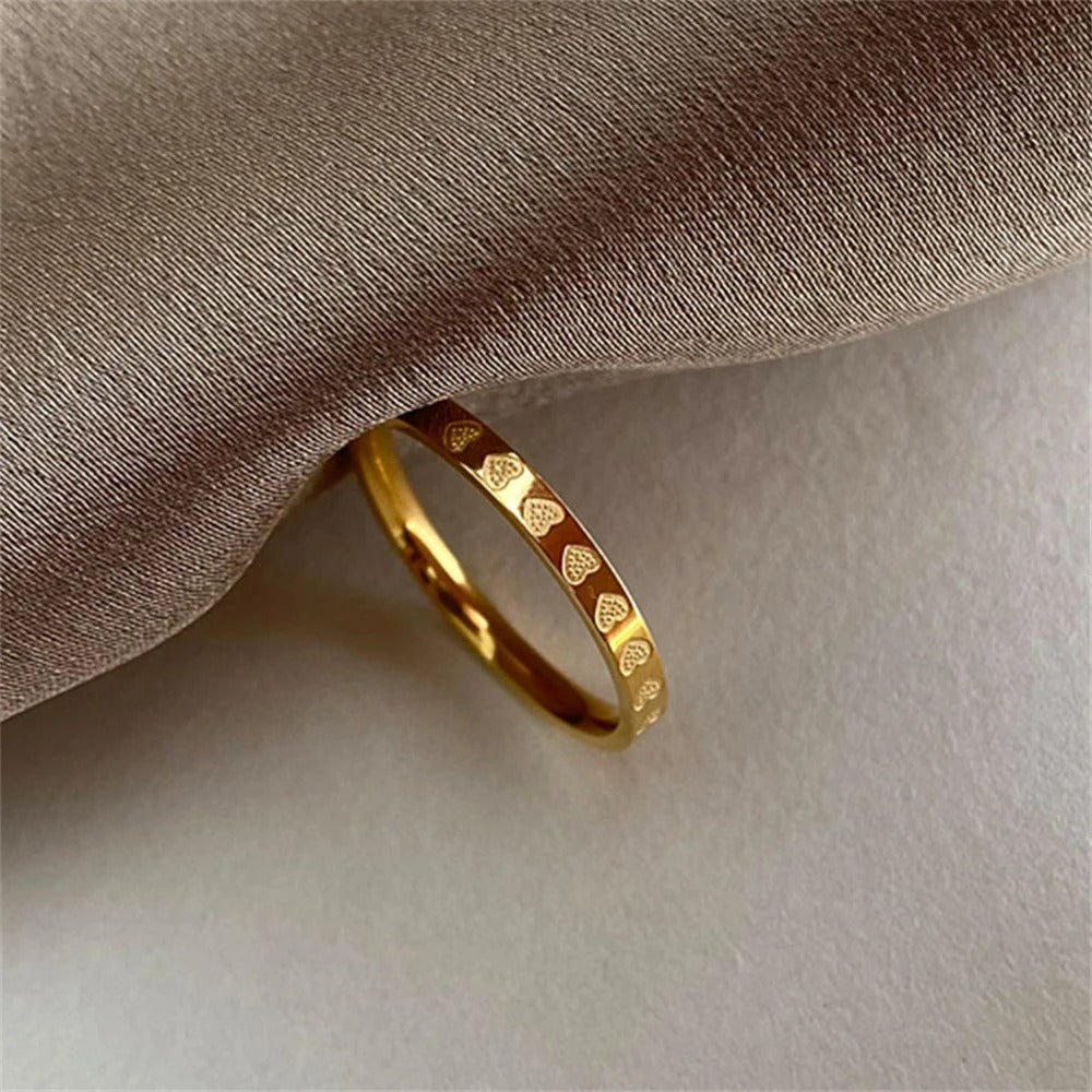Bague Femme Anneau Gravé Cœurs, doré présenté près d'un tissu beige