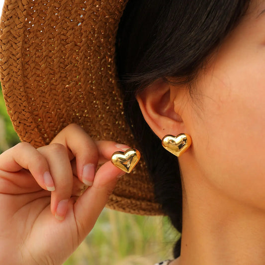 Boucle D'oreille Femme Cœur Minimaliste Doré, portée par une femme, l'autre boucle elle la présente entre ses doigts 
