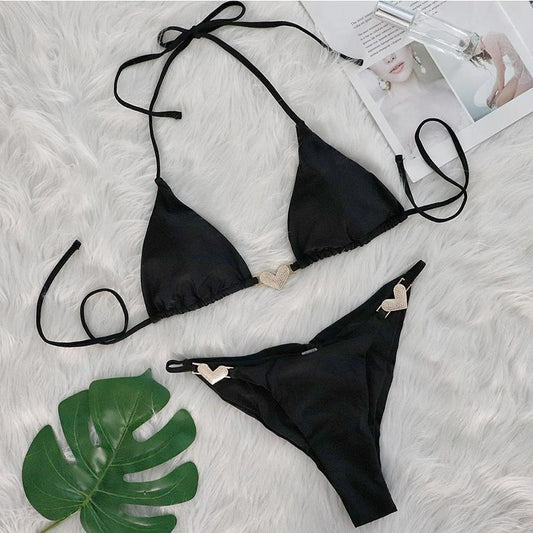 Maillot de Bain Femme Bijoux Cœurs Strass noir, présenté sur un tissu blanc en poils à côté d'une feuille de monstera